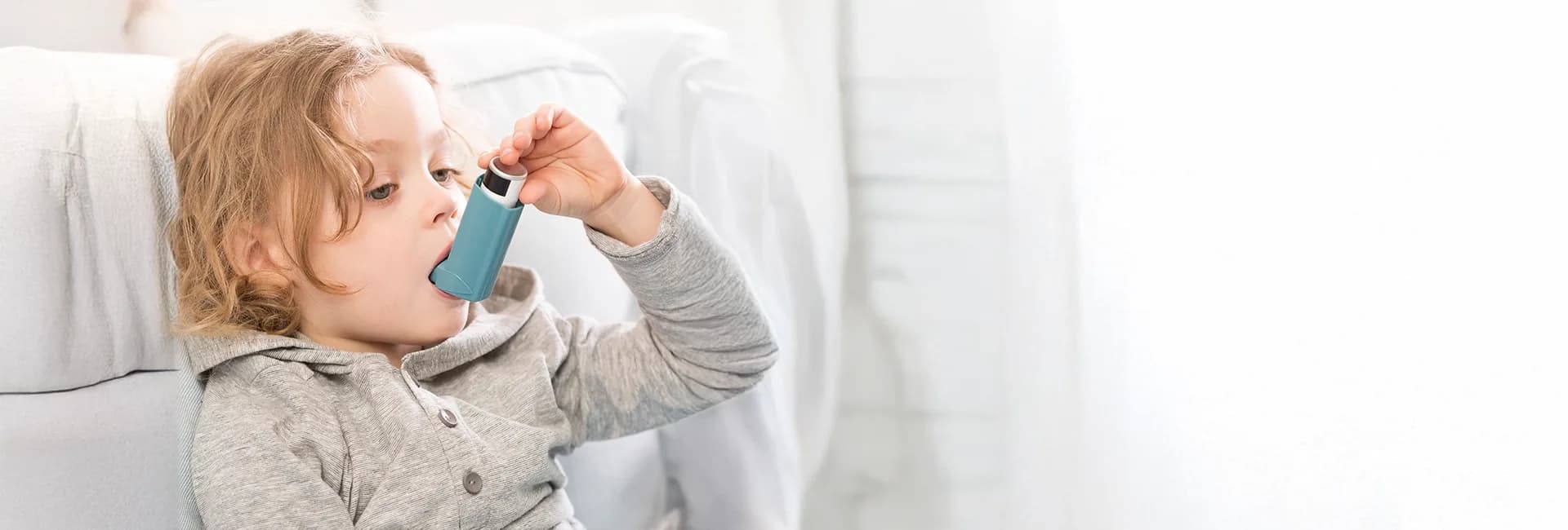 Young child using an inhaler on a sofa