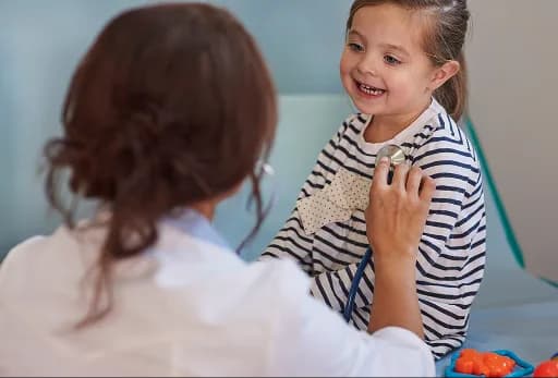 Paediatrician examining a smiling girl with a stethoscope