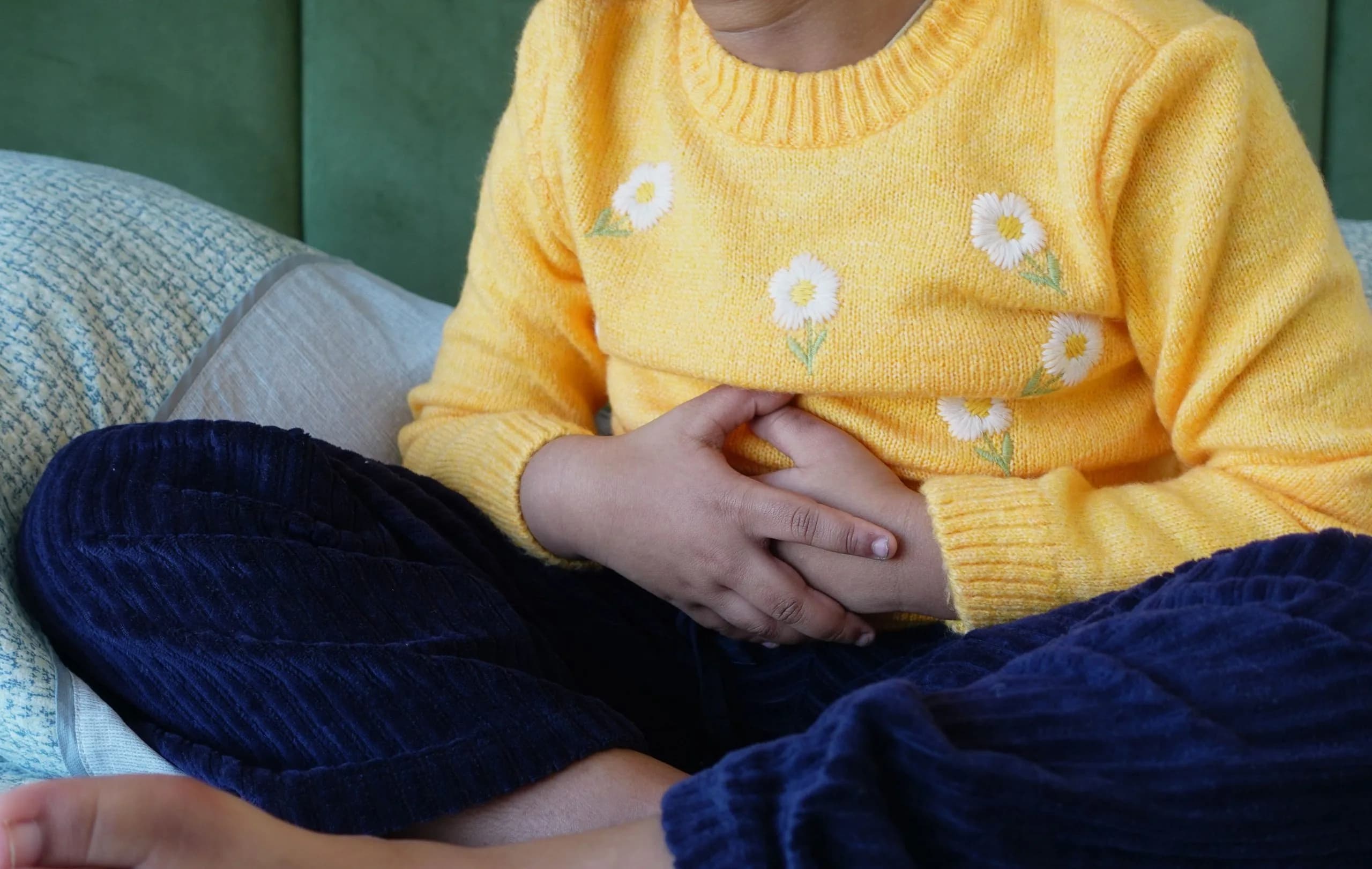 Child holding their tummy sitting cross-legged